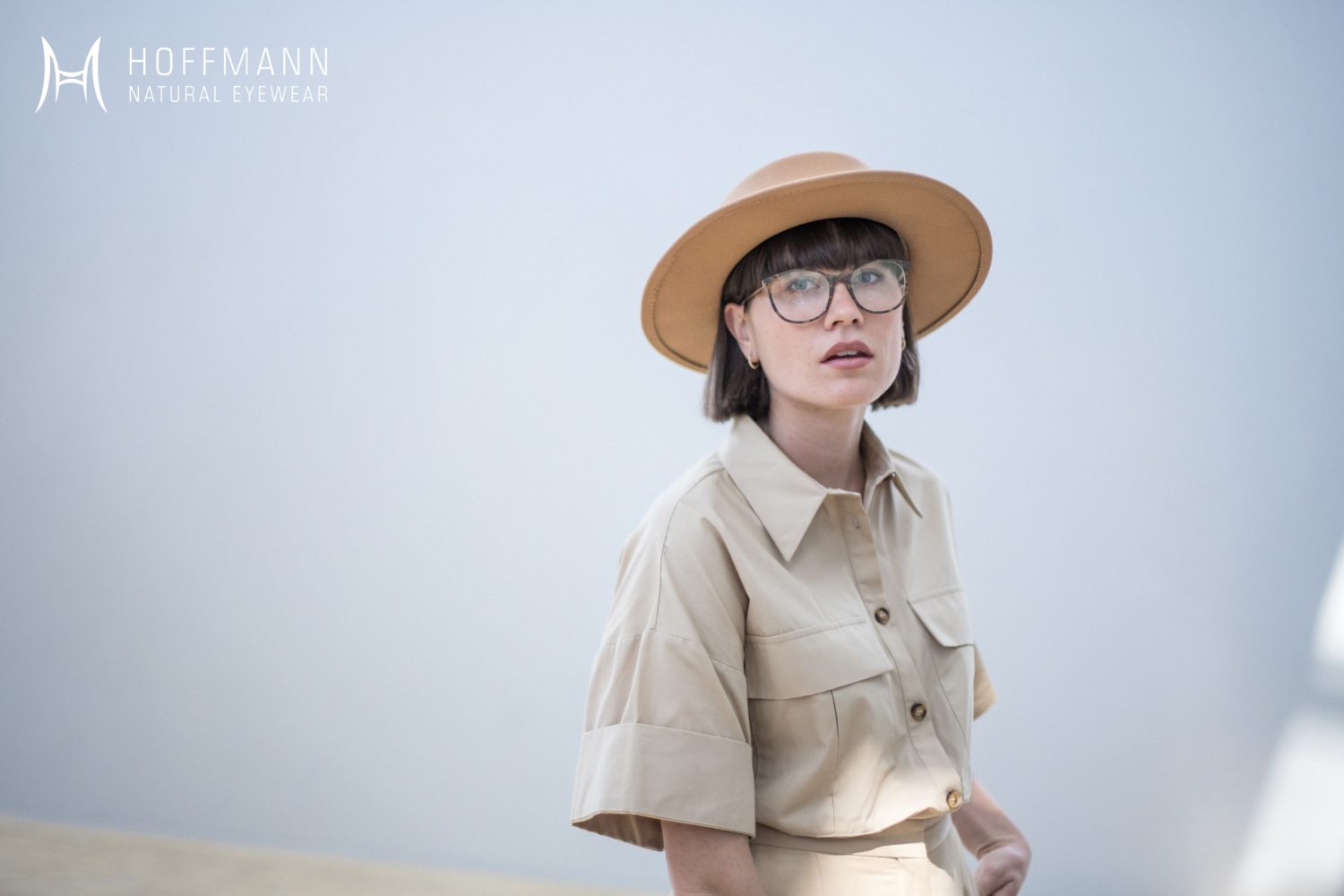 Eine junge Frau mit Safaribluse und Hut trägt eine Hornbrille von Hoffmann Natural Eyewear.